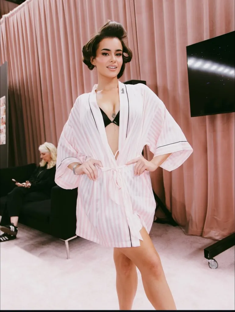 Barbie Ferreira in a pink and white striped robe and a black bra, with her hair in rollers.