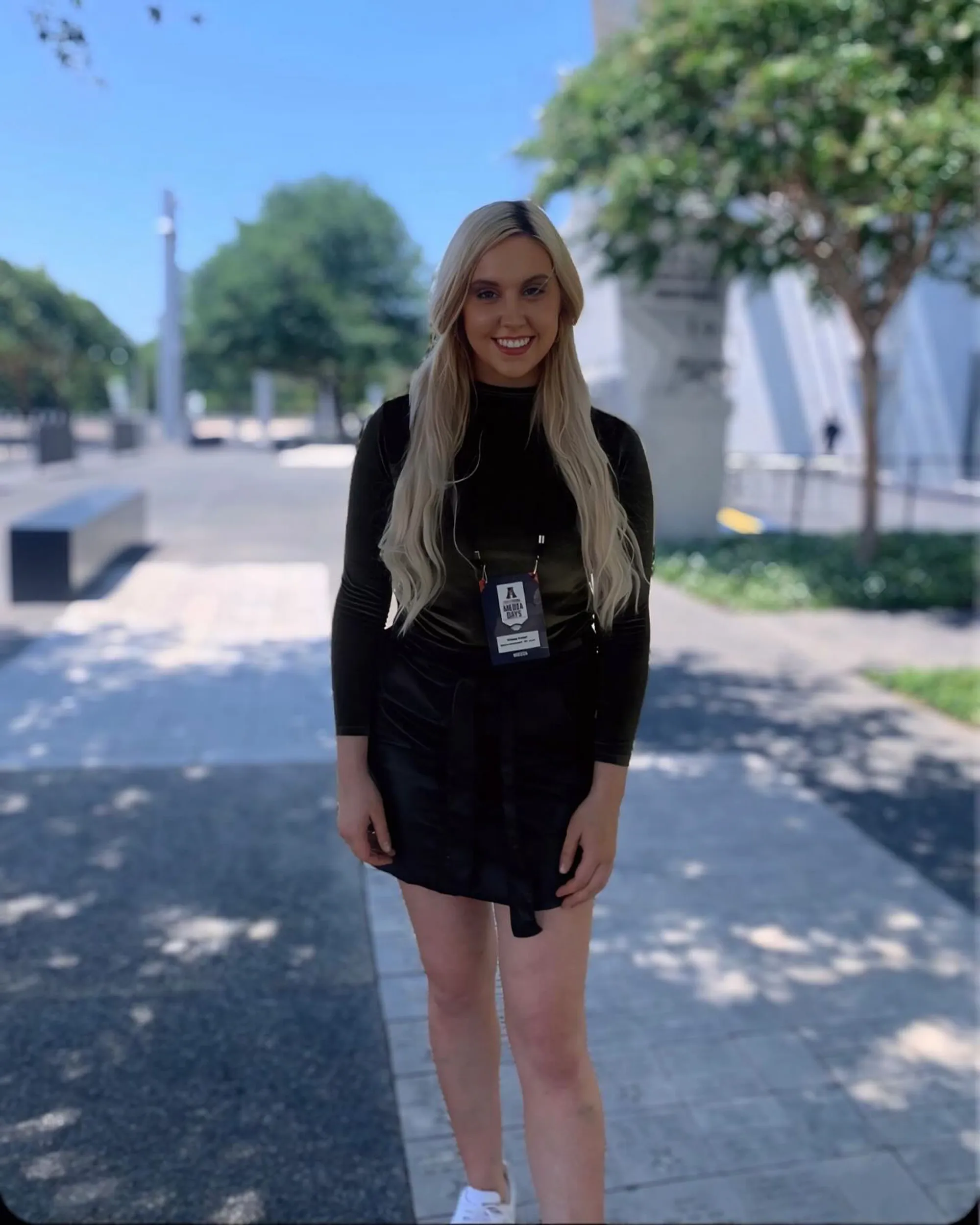 Crissy Froyd standing outside, wearing a black top and skirt with a "Media Days" pass.