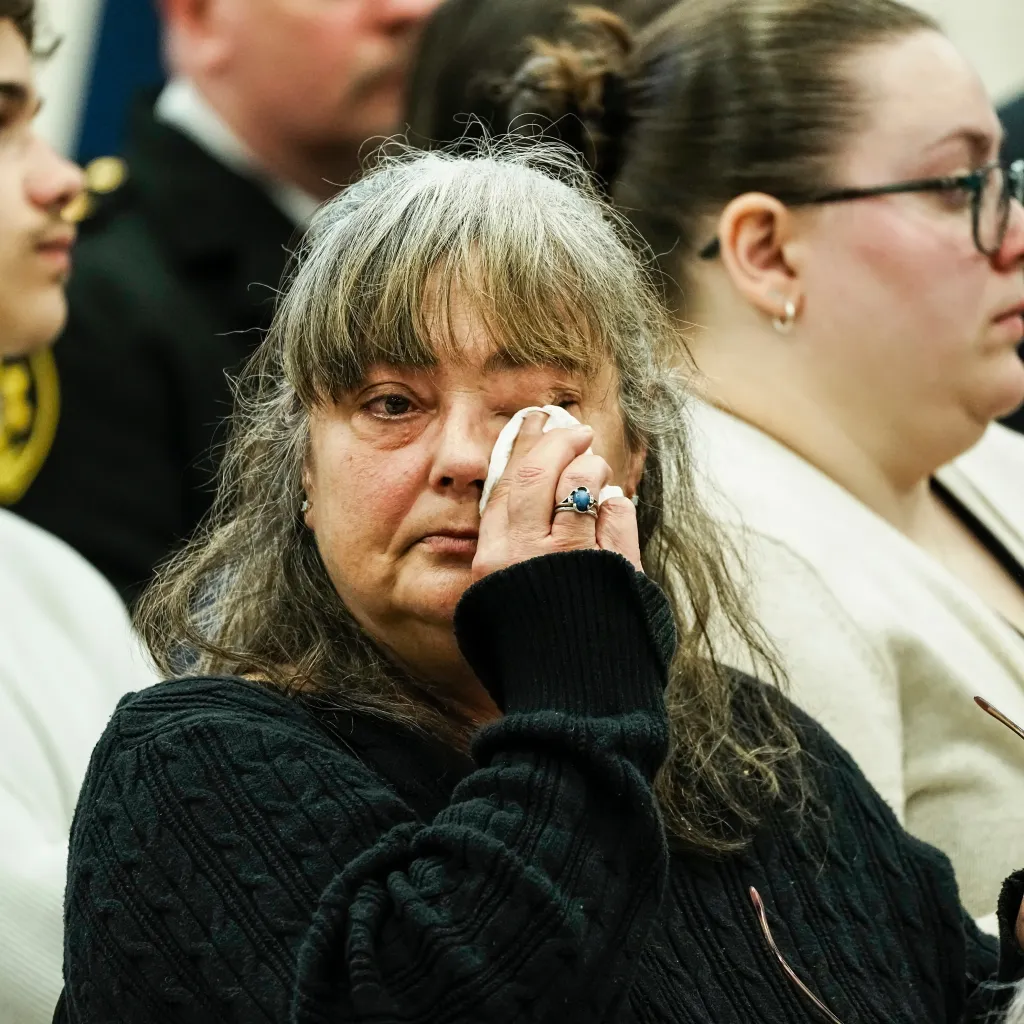 A woman with grey hair wiping her eye with a tissue during a news conference about the Gilgo Beach serial killings.
