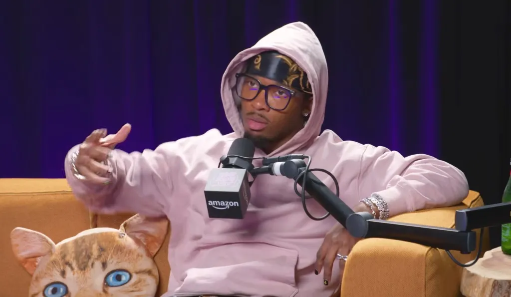 d4vd, in a pink hoodie, black glasses, and black durag, giving an interview.