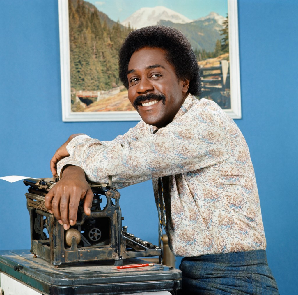 Demond Wilson as Lamont Sanford, smiling with his arm resting on an antique typewriter.