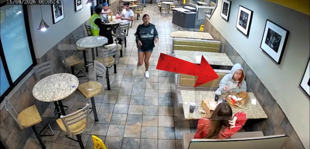 CCTV footage of a woman in a grey hoodie eating at a restaurant with another person, as another woman runs past them, highlighted by a red arrow.