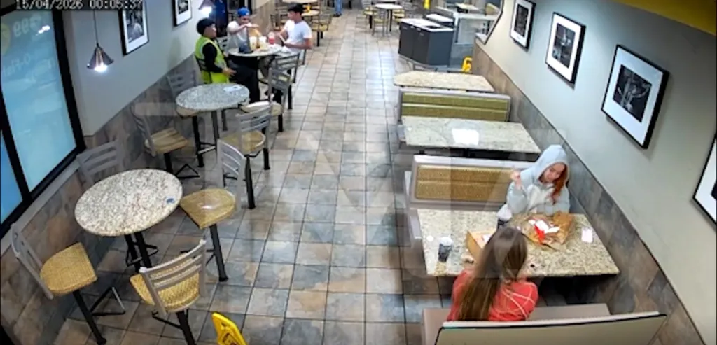 Ice Spice, wearing a gray hoodie, looking down at a table in a McDonald's.