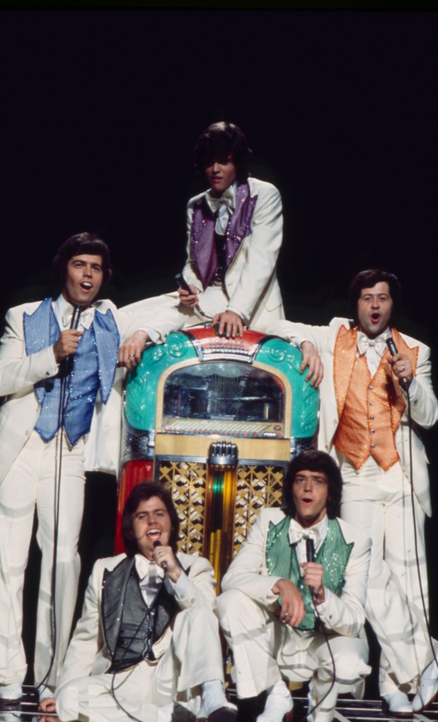 The Osmonds performing on stage in white suits and colorful vests around a jukebox.