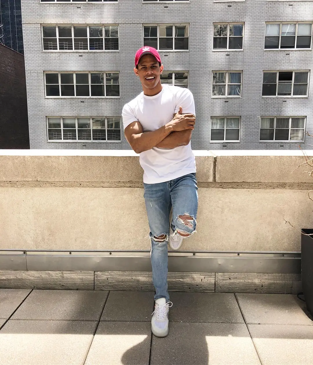 Donovan Michaels, a young man, in a white T-shirt, ripped jeans, and a red baseball cap, smiling with arms crossed.