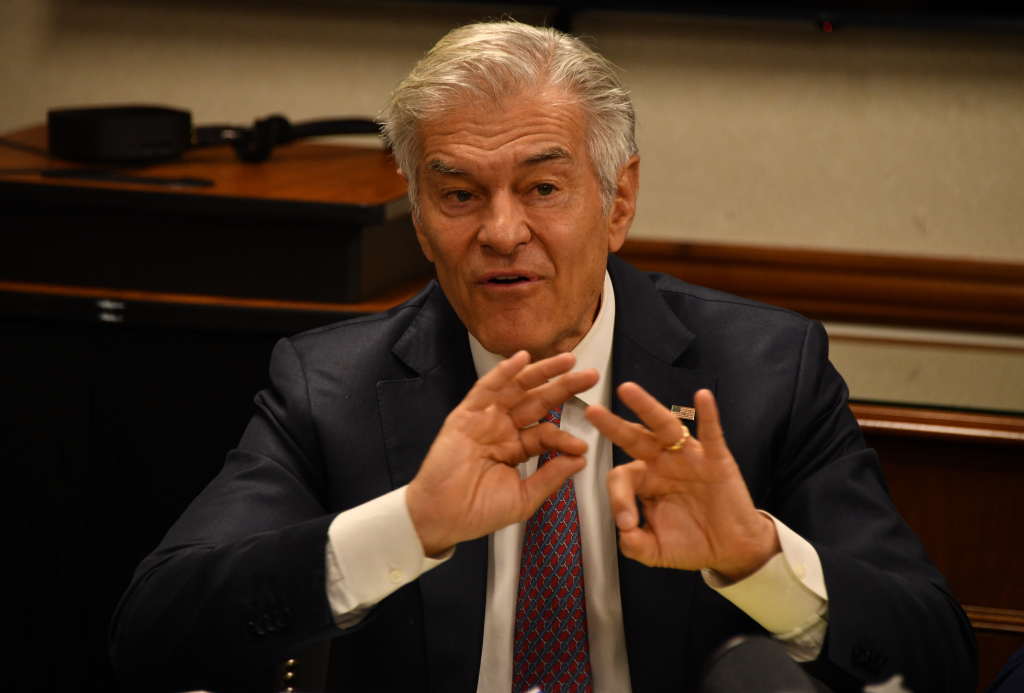 Dr. Mehmet Oz speaking at a press conference on fraud prevention, gesturing with both hands.