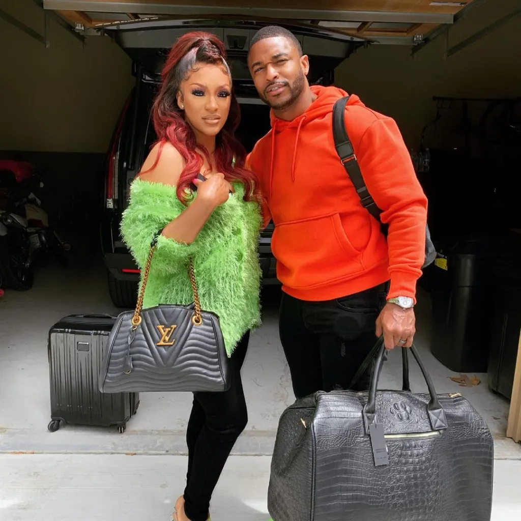 Drew Sidora and Ralph Pittman standing in a garage with luggage.