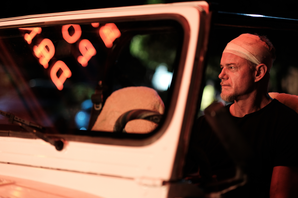 Eric Dane in season 2 of Euphoria, wearing a head bandage while looking out a car window at night.