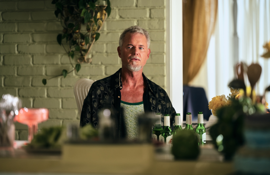 Eric Dane from Euphoria Season 3 looks at the camera while sitting at a table with beer bottles.