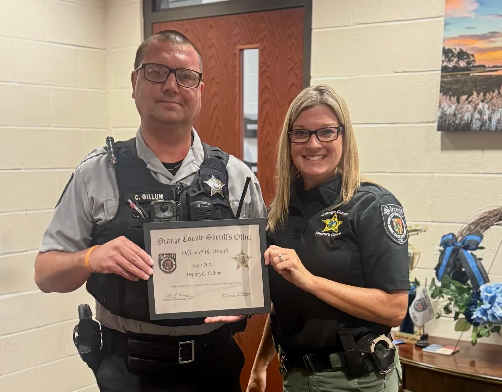 Two police officers, a man and a woman, holding up an "Officer of the Month" award for Deputy C. Gillum.