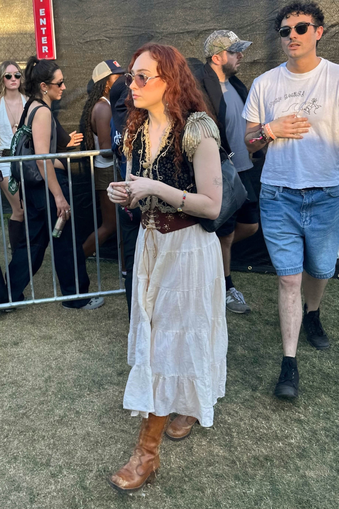 Chappell Roan at the Coachella Music Festival, wearing a black and gold vest, a long white skirt, and brown boots.