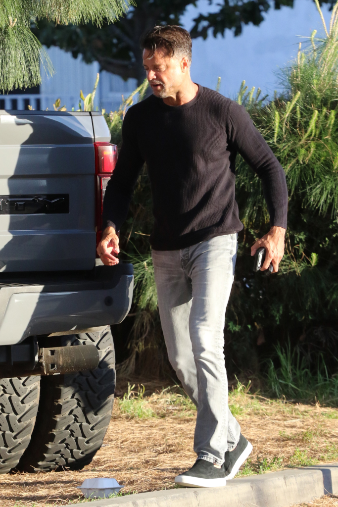 David Charvet walks next to a vehicle, wearing a black shirt and light-colored pants.