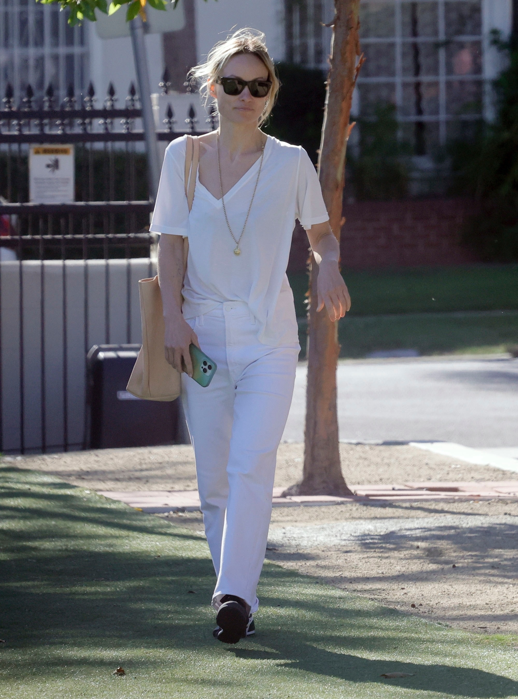 Olivia Wilde walking while wearing a white outfit and sunglasses.