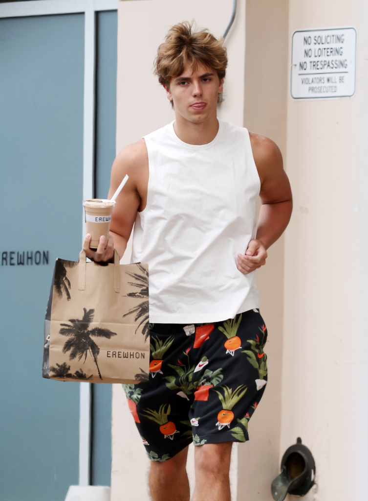 Jayden Federline wearing a white tank top and patterned shorts, carrying an Erewhon grocery bag and drink.