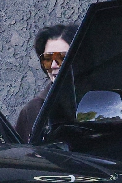 Kris Jenner in sunglasses and dark hair, peeking from behind a car door.