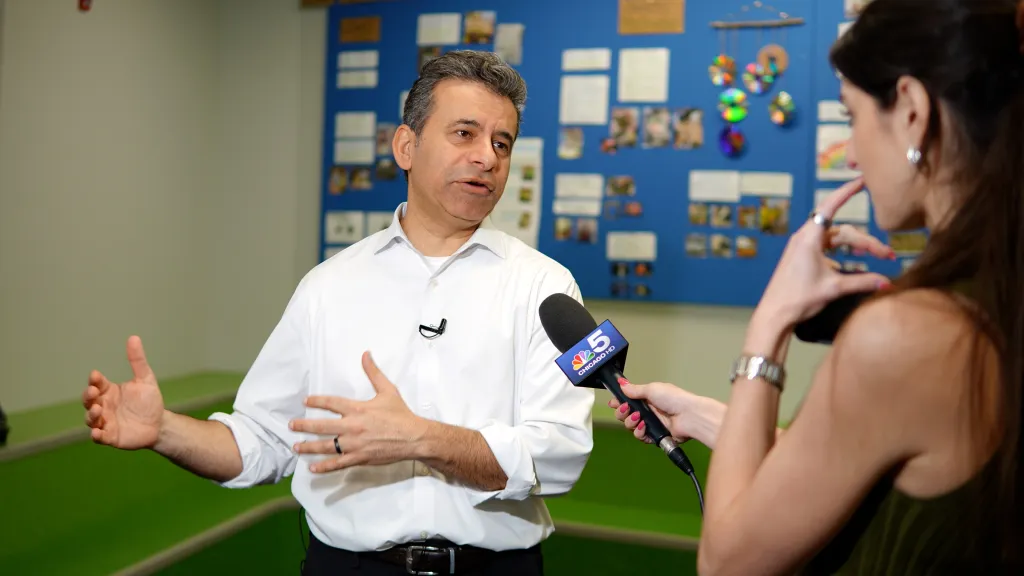 A man in a white shirt and black pants gives an interview to a reporter holding a microphone with a Channel 5 Chicago logo.