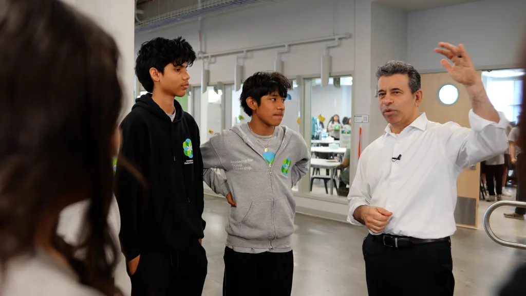 A man in a white shirt speaks to two boys in hoodies with the "Academy for Global Citizenship" logo.