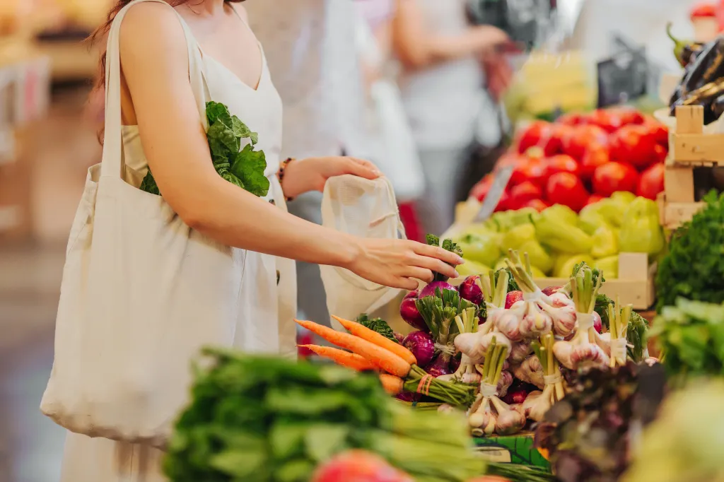 A woman places vegetables into a reusable produce bag at a food market.