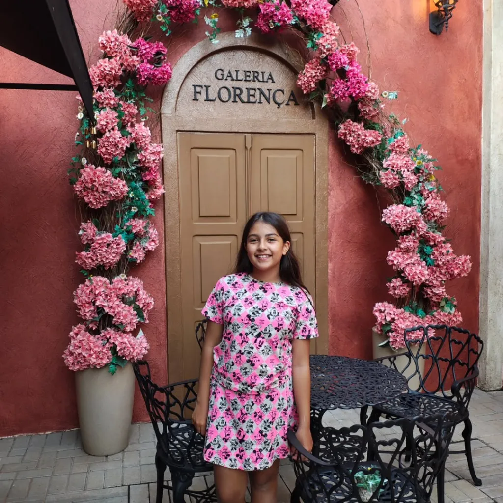 Laura Pereira Camargo smiling in front of a door decorated with pink flowers.