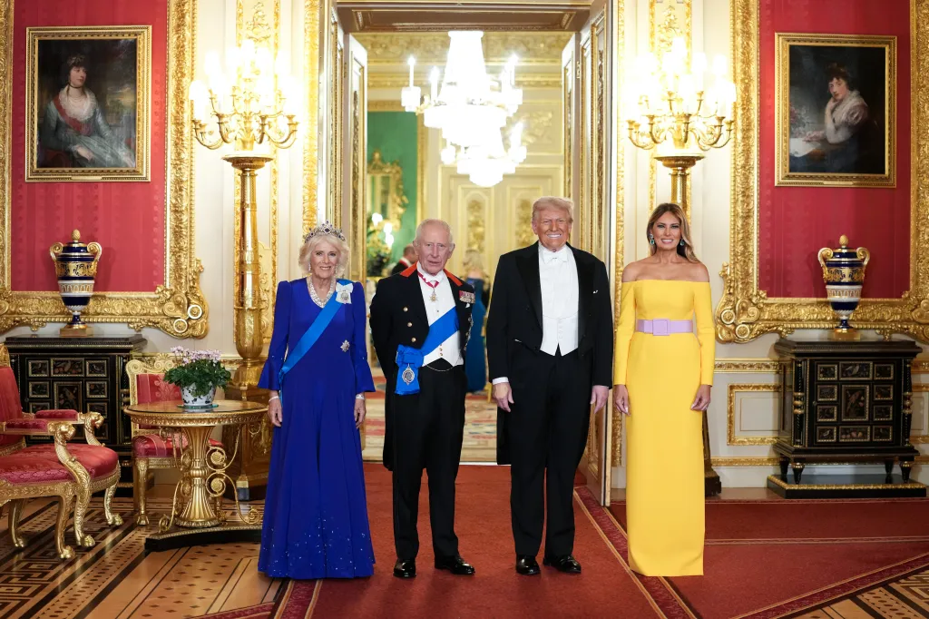 Queen Camilla, King Charles III, Donald Trump, and Melania Trump stand in a grand room with red and gold decor.