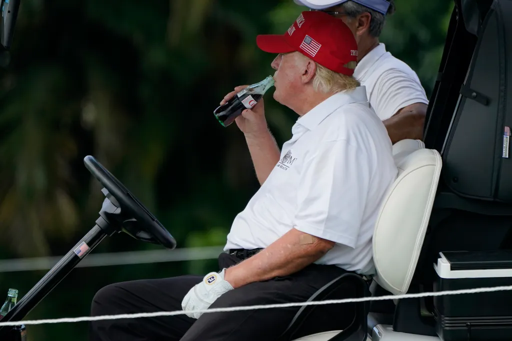 Donald Trump drinking a Diet Coke in a golf cart.