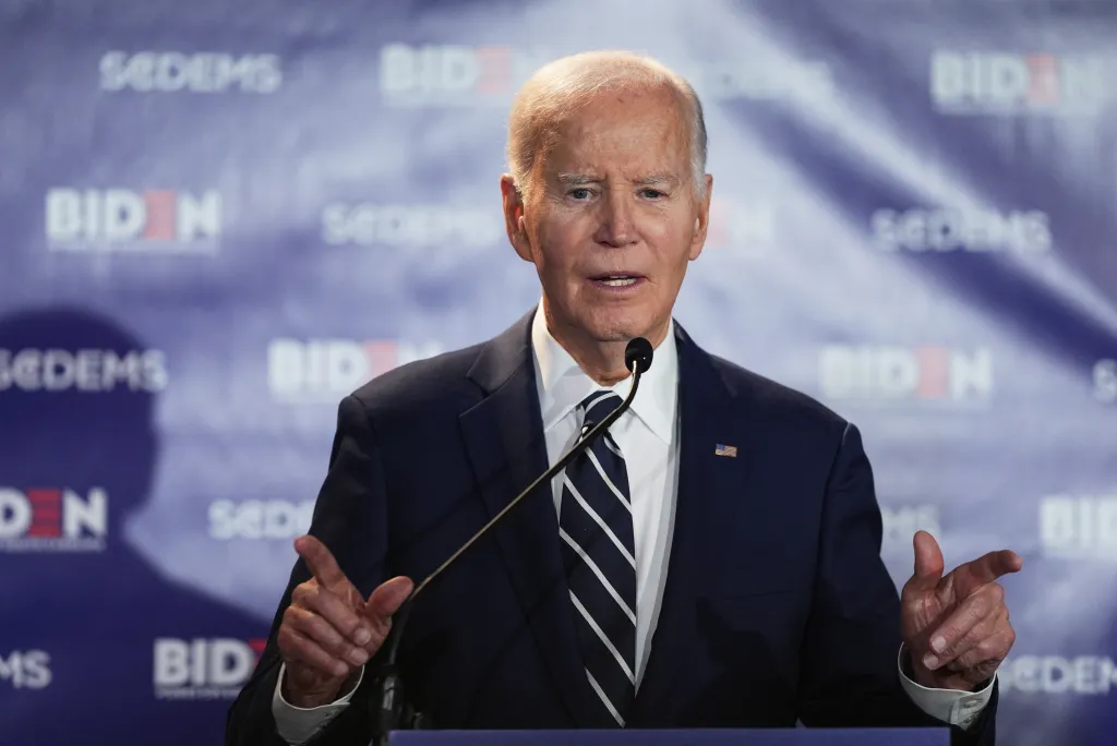 Joe Biden speaking at a podium with a "Biden" backdrop.