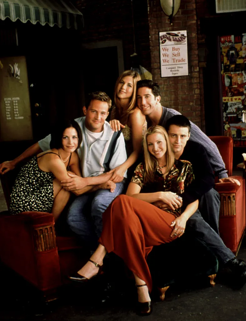 The cast of Friends, including Courteney Cox, Matthew Perry, Jennifer Aniston, David Schwimmer, Lisa Kudrow, and Matt LeBlanc, posing together on a red couch.
