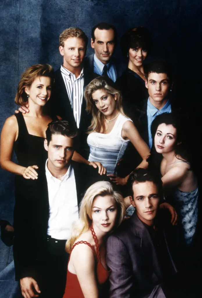 Cast photo of "Beverly Hills, 90210". From left: Gabrielle Carteris, in a black dress, Ian Ziering, in a black jacket, black and white striped shirt, James Eckhouse, in a grey suit, Carol Potter, in a black dress, Brian Austin Green, in a blue shirt and black jacket, Shannen Doherty, in a blue dress, Luke Perry, in a grey blazer, Jennie Garth, in a red dress, Jason Priestley, in a black jacket, black pants and white shirt, and Tori Spelling, in a white dress.
