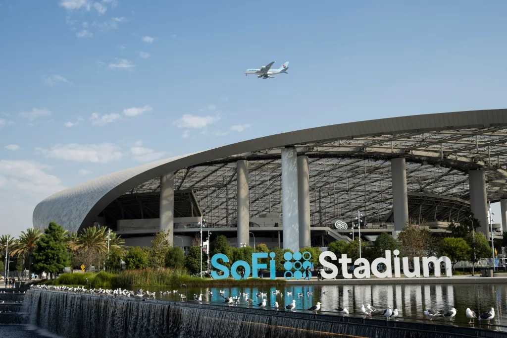 Exterior view of SoFi Stadium with the SoFi Stadium sign and a plane overhead.