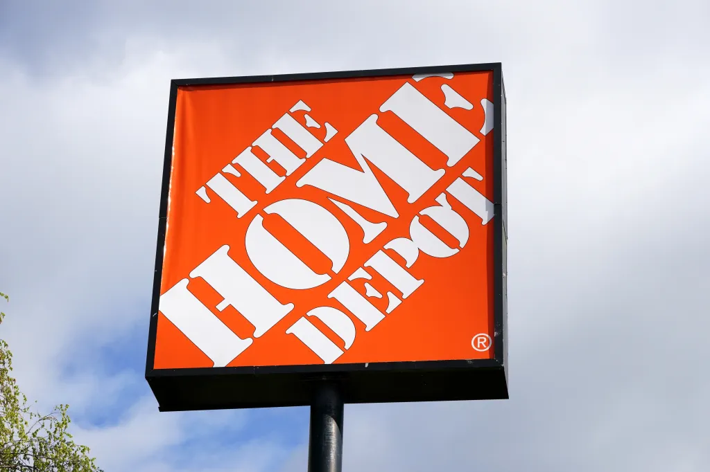 The Home Depot sign, in orange and white, stands against a cloudy sky.