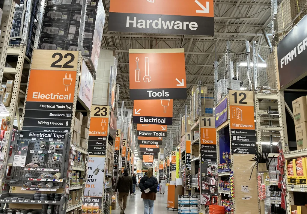 Interior view of a Home Depot store with several aisles of products and overhead signage, including "Hardware", "Tools", and "Electrical".