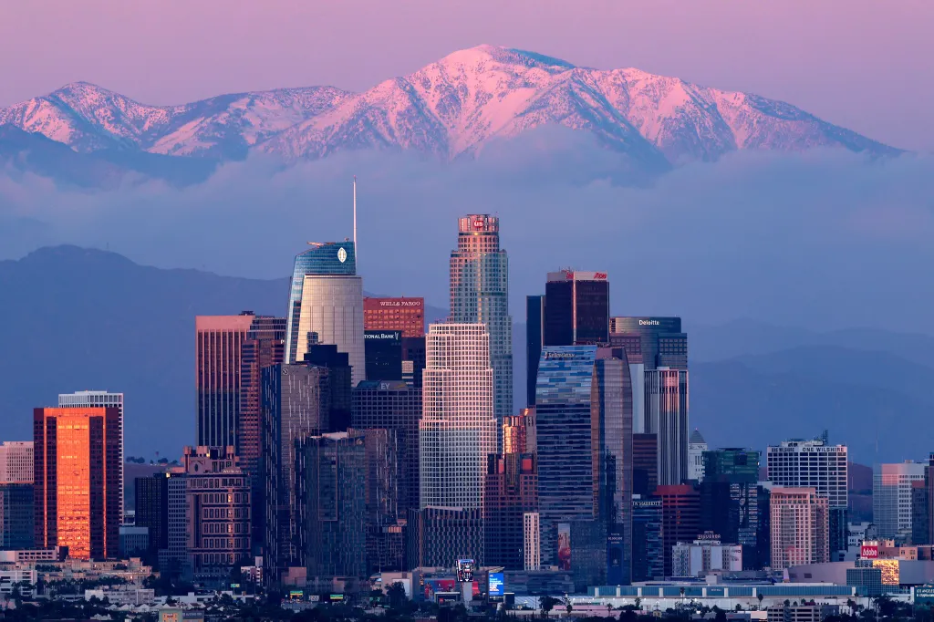 Los Angeles downtown skyline with snow-capped mountains in the background at sunset.