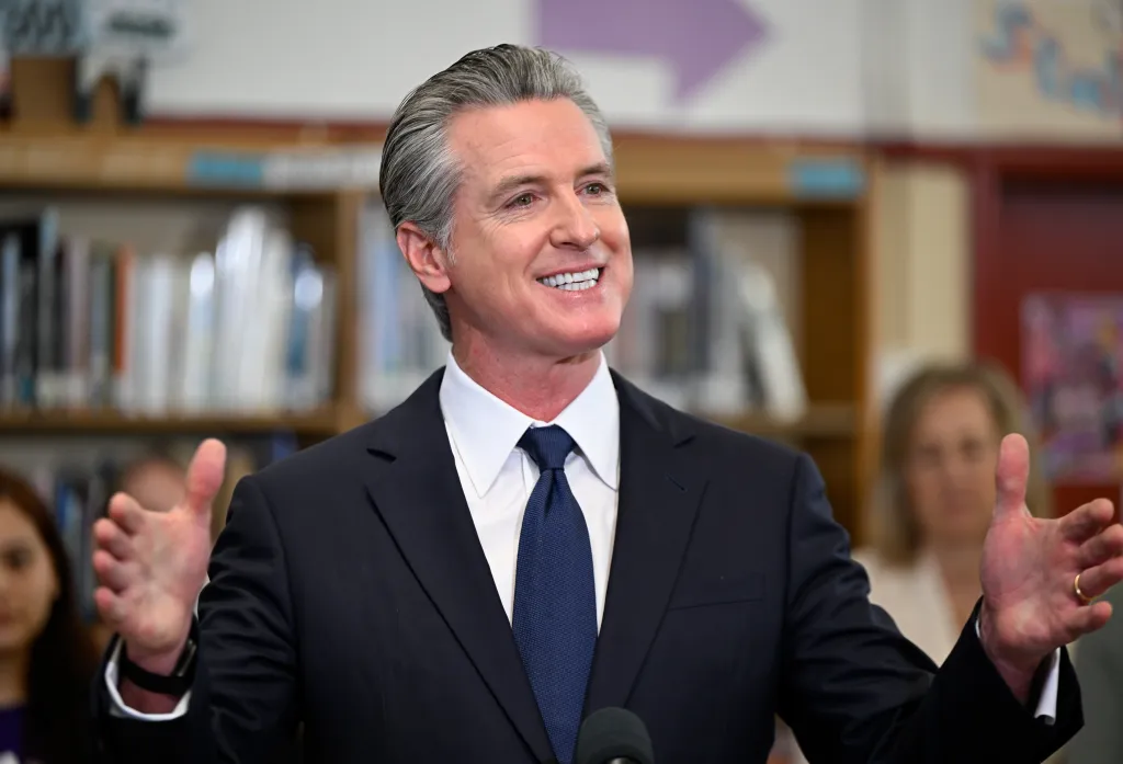 Governor Gavin Newsom speaking at a press conference with his hands raised.