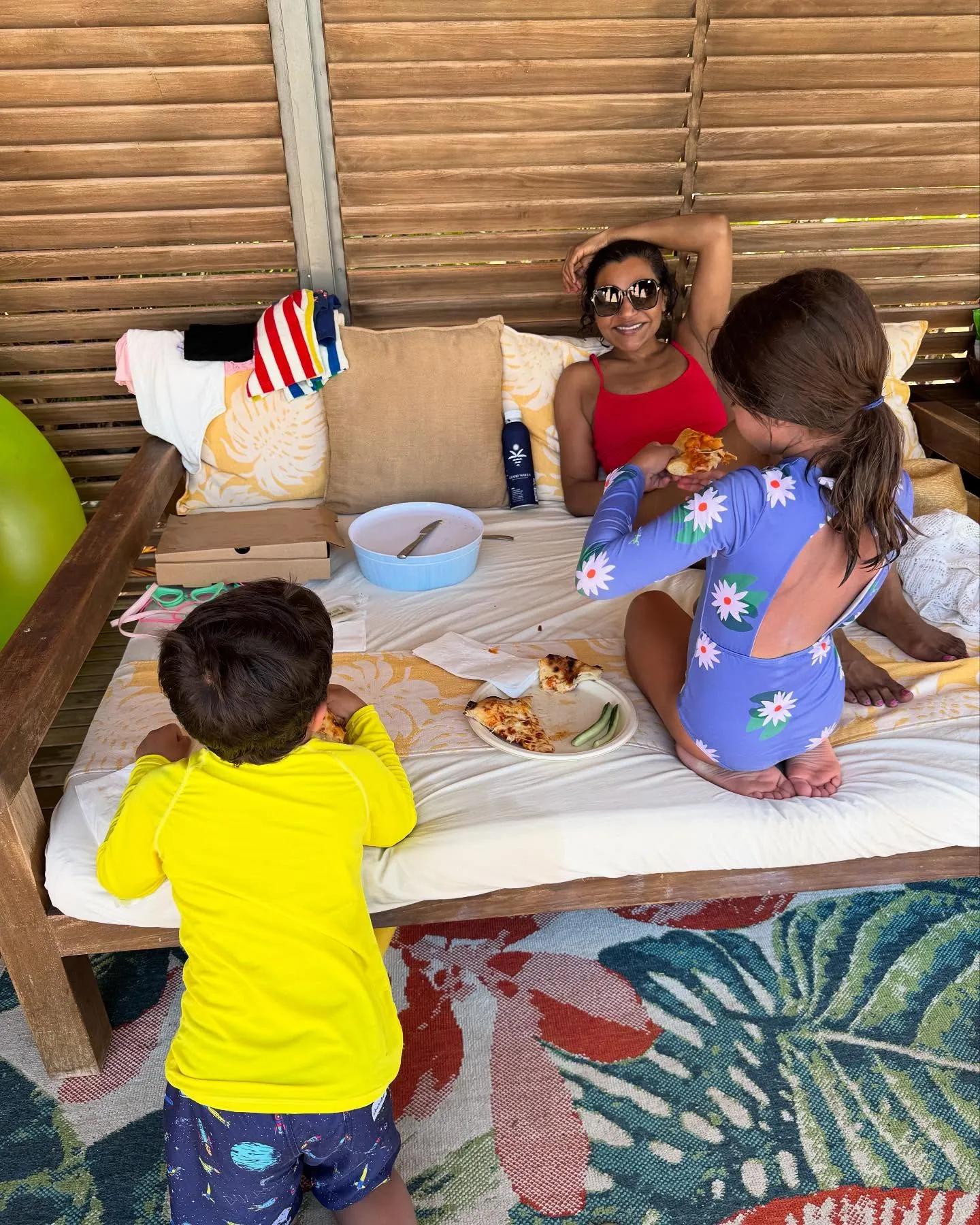 Mindy Kaling relaxing on a daybed with her two children, eating pizza.