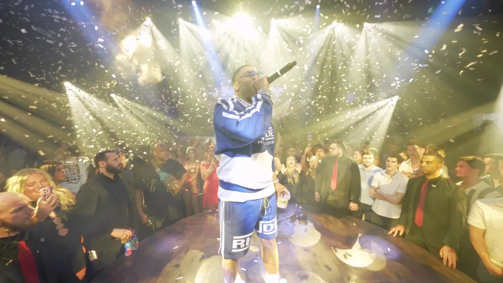 Nelly performing on a table at E11even Miami, surrounded by a cheering crowd and falling confetti.