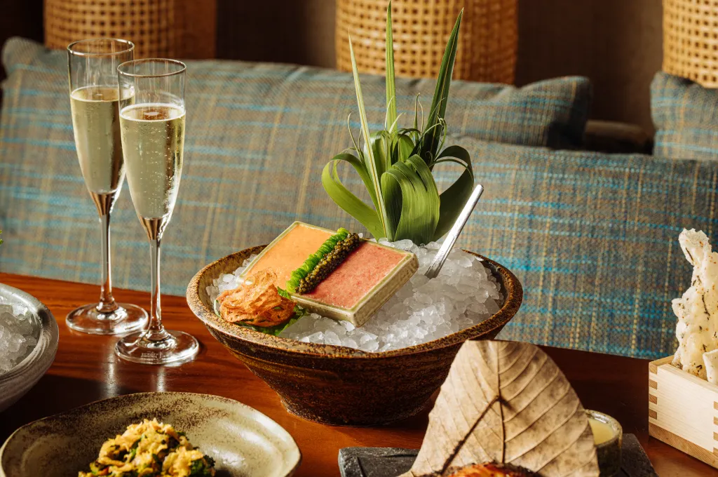 Two champagne flutes and a bowl of caviar and other dishes on a wooden table.