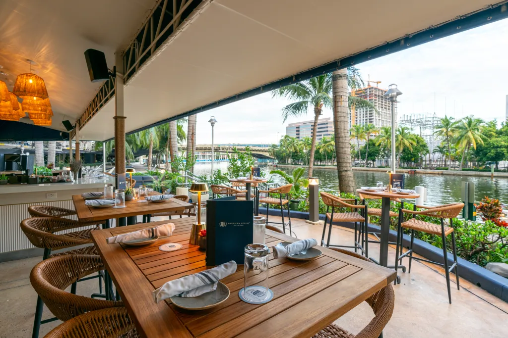 Outdoor dining area at American Social Bar & Kitchen with tables and chairs set on a patio overlooking a canal.