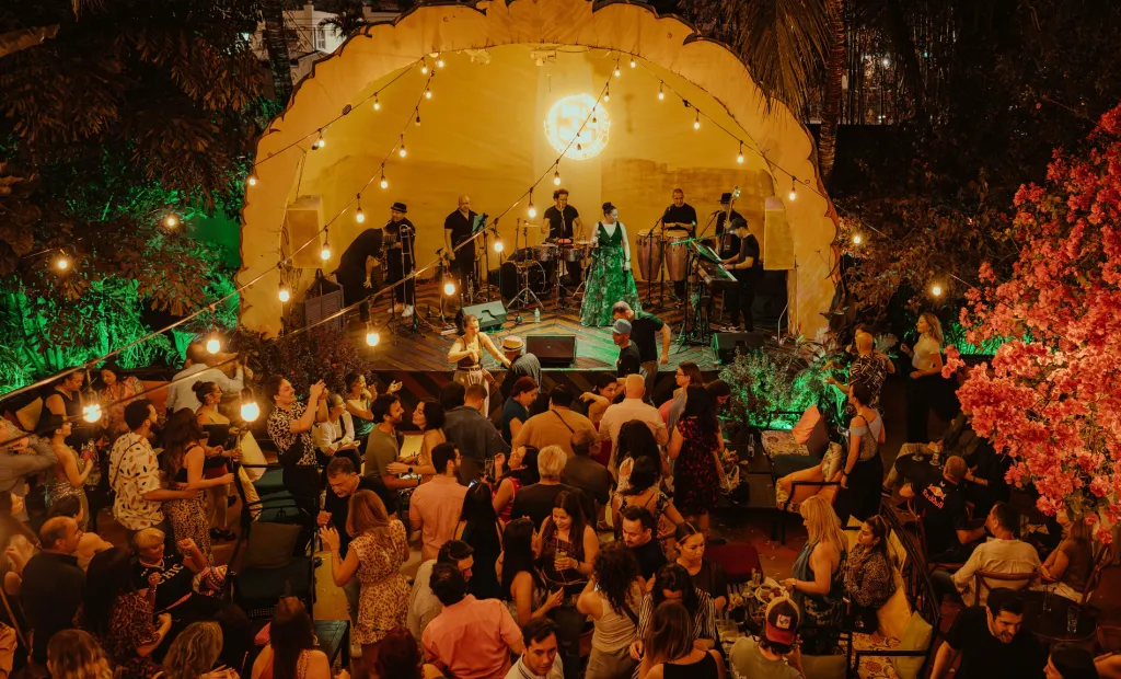 A live band performing on a stage while people dance and socialize at an outdoor evening event.