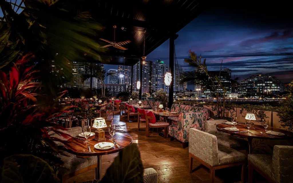 Delilah Miami's outdoor dining area at night, featuring a cityscape in the background.