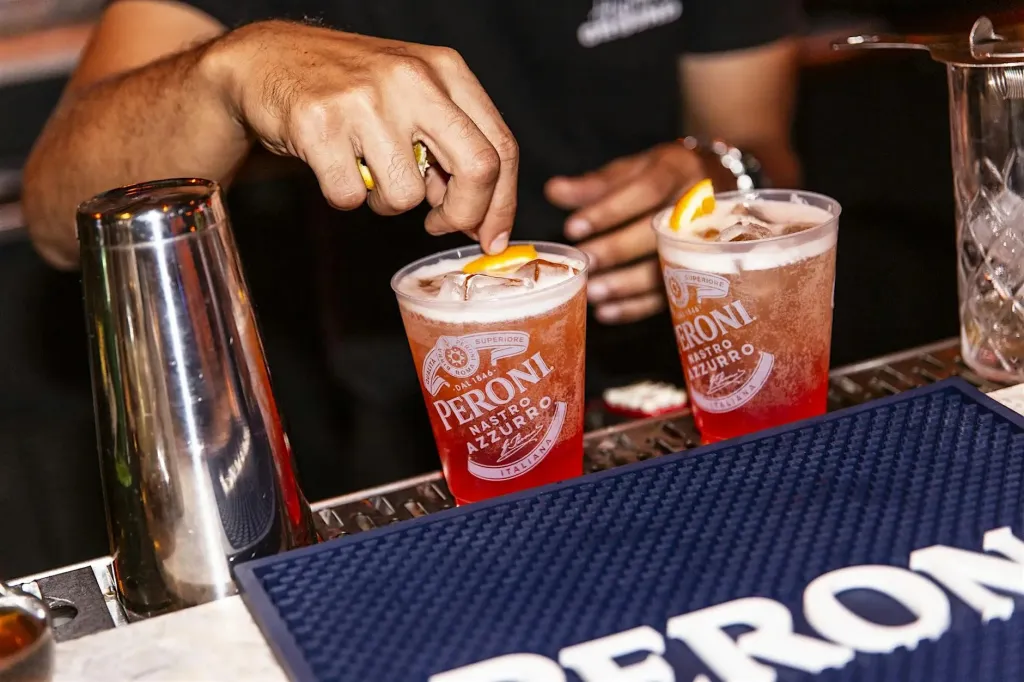 A bartender garnishes a Peroni Nastro Azzurro drink with an orange slice.