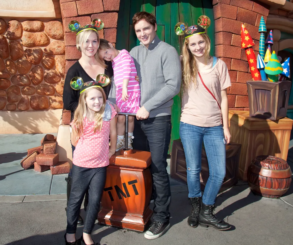 From left: Jennie Garth , in Mickey Mouse ears and. black dress, holding daughter Fiona Facinelli, in a pink and white striped dress, daughter Lola Facinelli wears a pink and white spotted t-shirt, Mickey Mouse ears and black pants, Peter Facinelli wears a grey sweater and jeans, Luca Facinelli wears a pink T-shirt, jeans and Mickey Mouse ears.