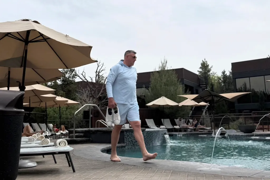 Mike Vrabel walking barefoot by a pool, holding white sneakers, at Ambiente Sedona hotel.
