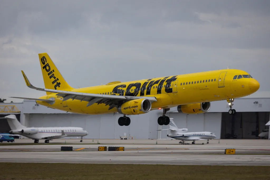 A yellow Spirit Airlines flight with "Spirit" written in black on its fuselage, landing at Fort Lauderdale - Hollywood International Airport.