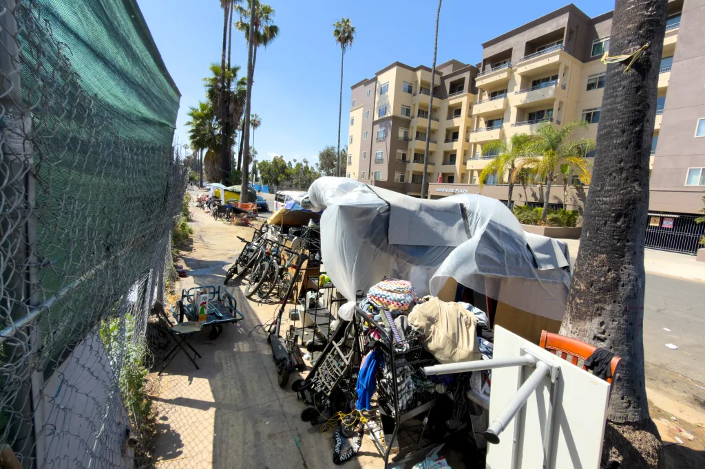 Homeless encampment on a sidewalk across from a building that reads "Arapahoe Plaza".