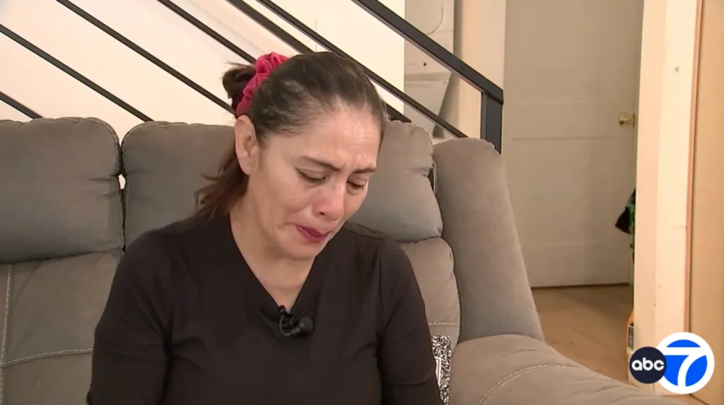 A woman with tears in her eyes looks down, distraught.