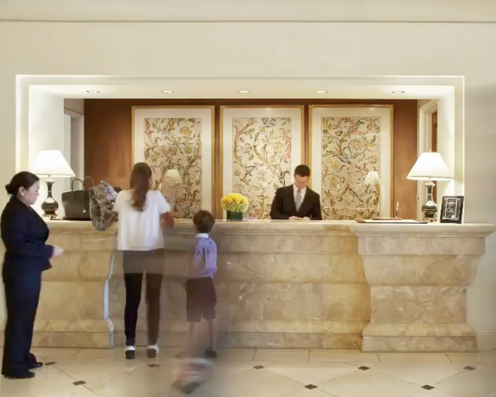 The Peninsula Beverly Hills hotel reception desk with a clerk, a woman, and a child.