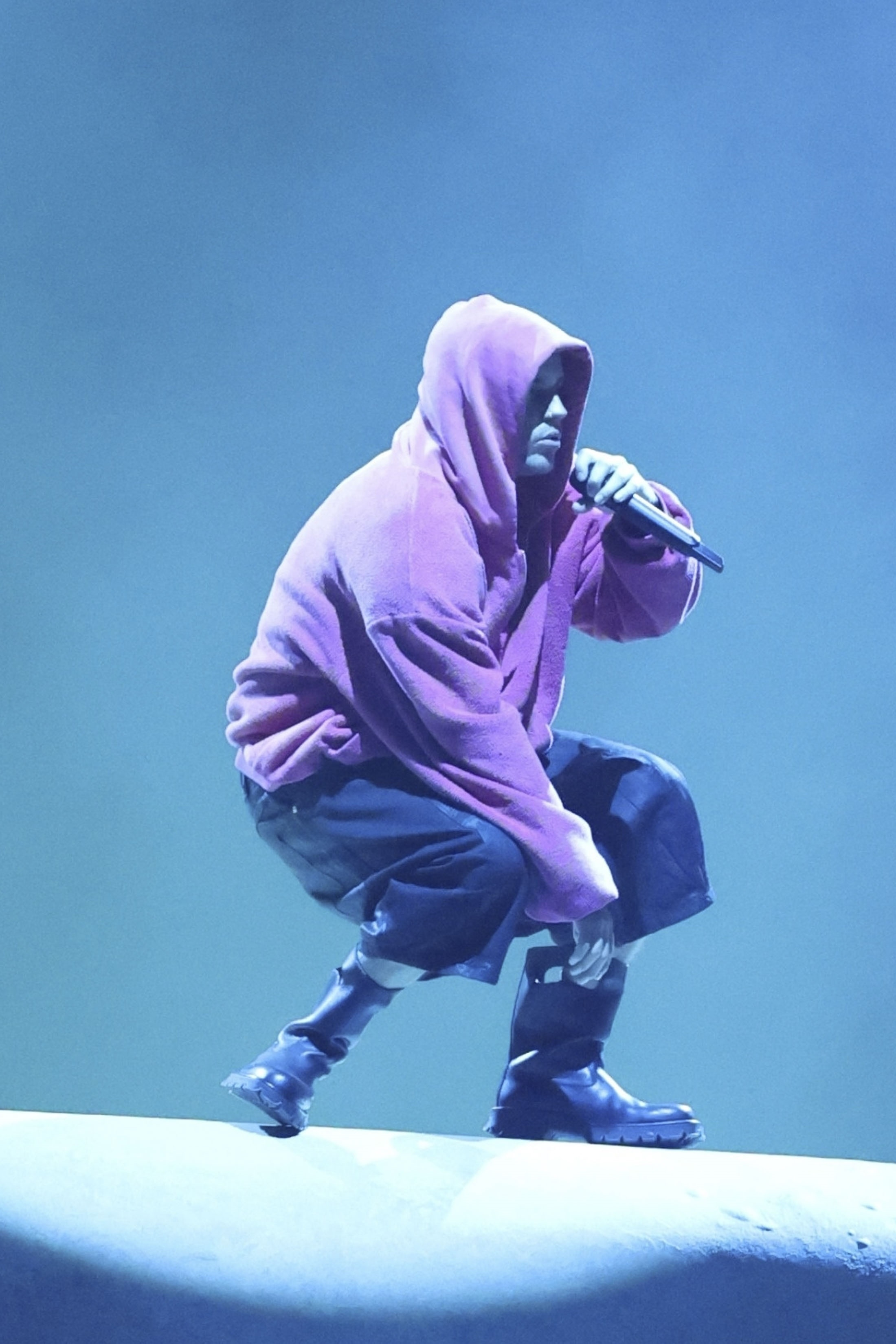 Justin Bieber performing at Coachella Music Festival, wearing a purple hooded robe and dark boots, while holding a microphone.