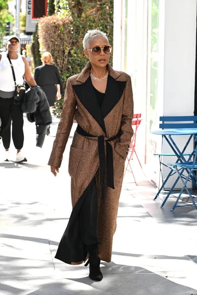 Jada Pinkett Smith walking outside in a brown and black patterned coat.