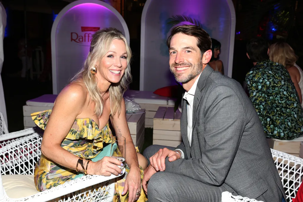 Jennie Garth, in a yellow floral strapless dress, and Dave Abrams, in a grey suit and white shirt, smiling at the Raffaello Summer Day event.