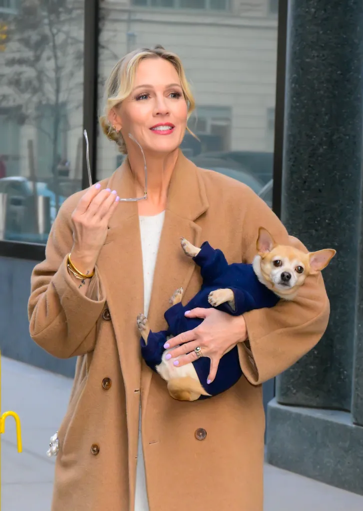 Jennie Garth in a tan coat, holding a chihuahua in a blue coat, outside "ABC Studio".
